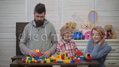 在游戏室的年轻家庭。 热爱家庭观念。 妈妈，爸爸和男孩用塑料积木搭建玩具。 父母和儿子